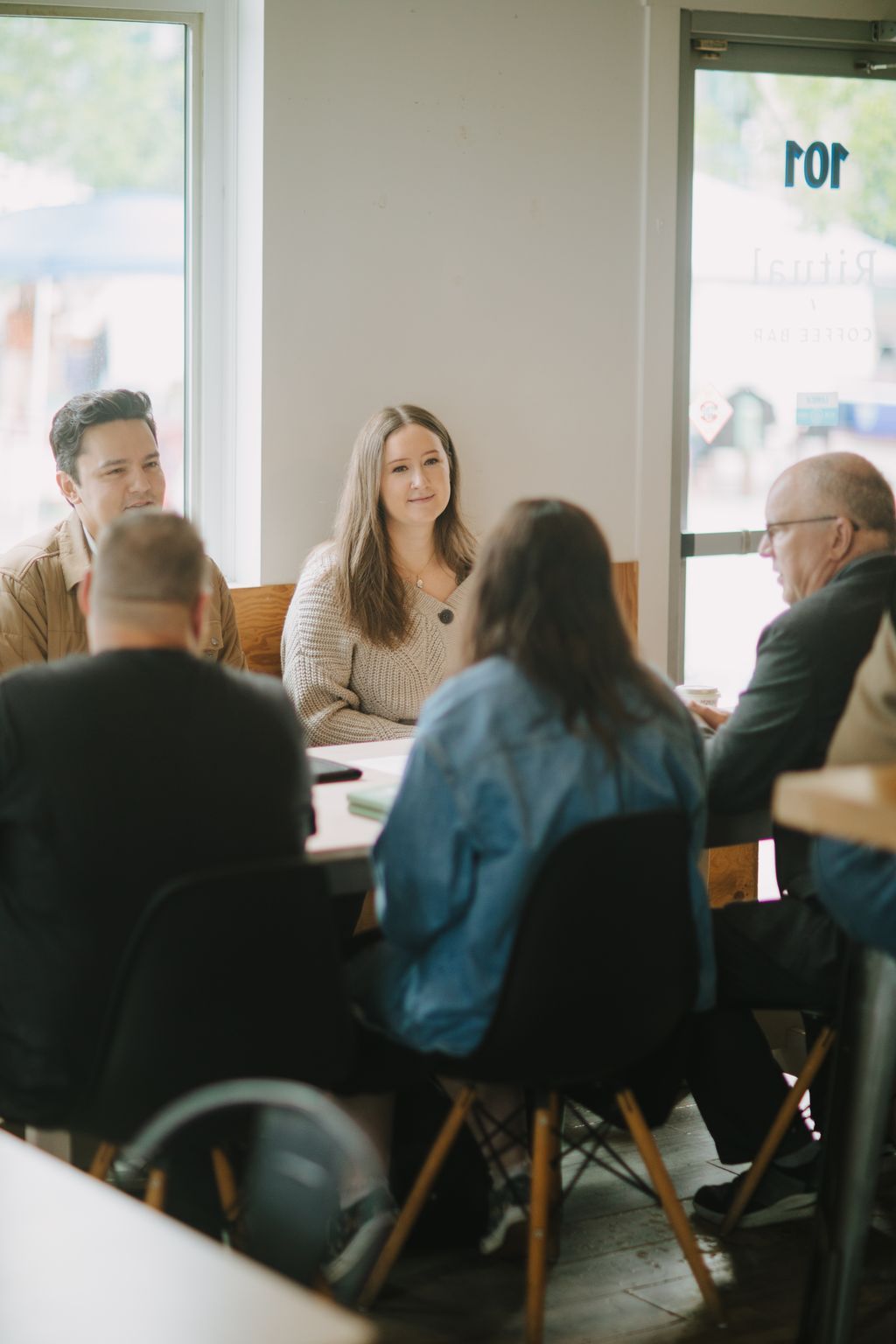 Woman in cream knit sweater smiles across table at person in blue jacket during intimate indoor conversation