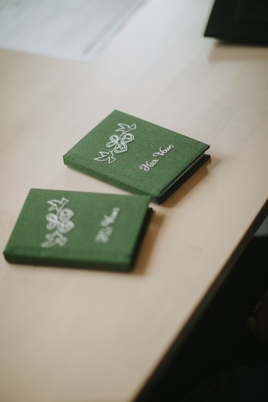 Green linen wedding vows books with white embroidered details and black binding on cream background