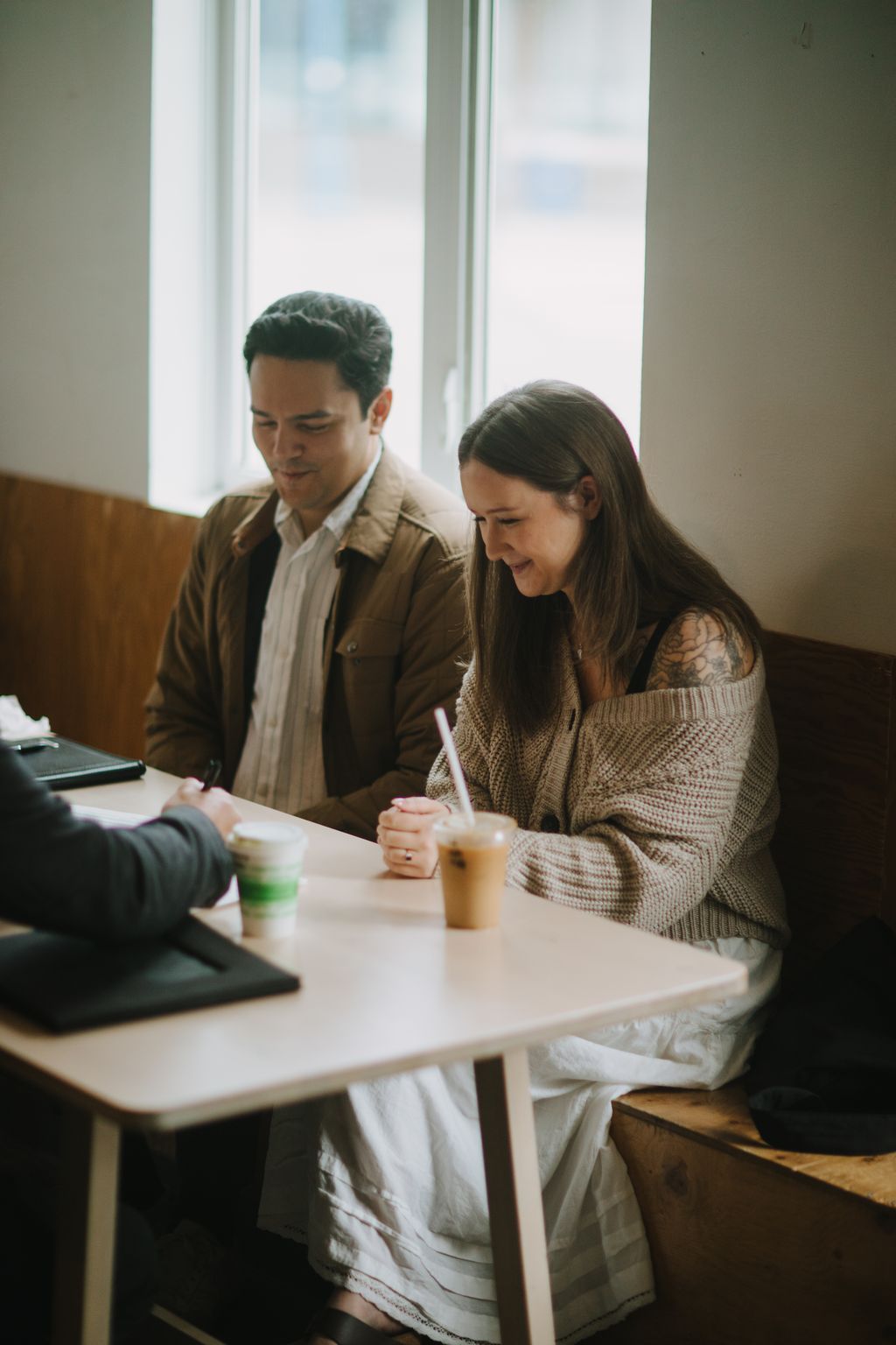 Couple smiling while looking at tablet by bright windows, warm neutral tones, intimate daytime setting