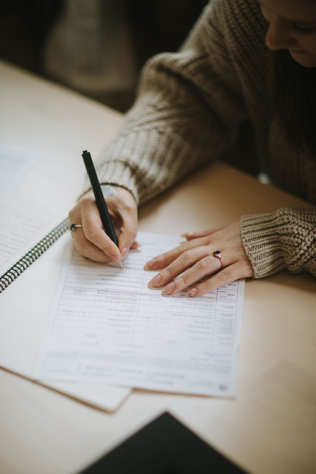 Bride in knit sweater signing marriage license with pen, diamond ring visible on her hand