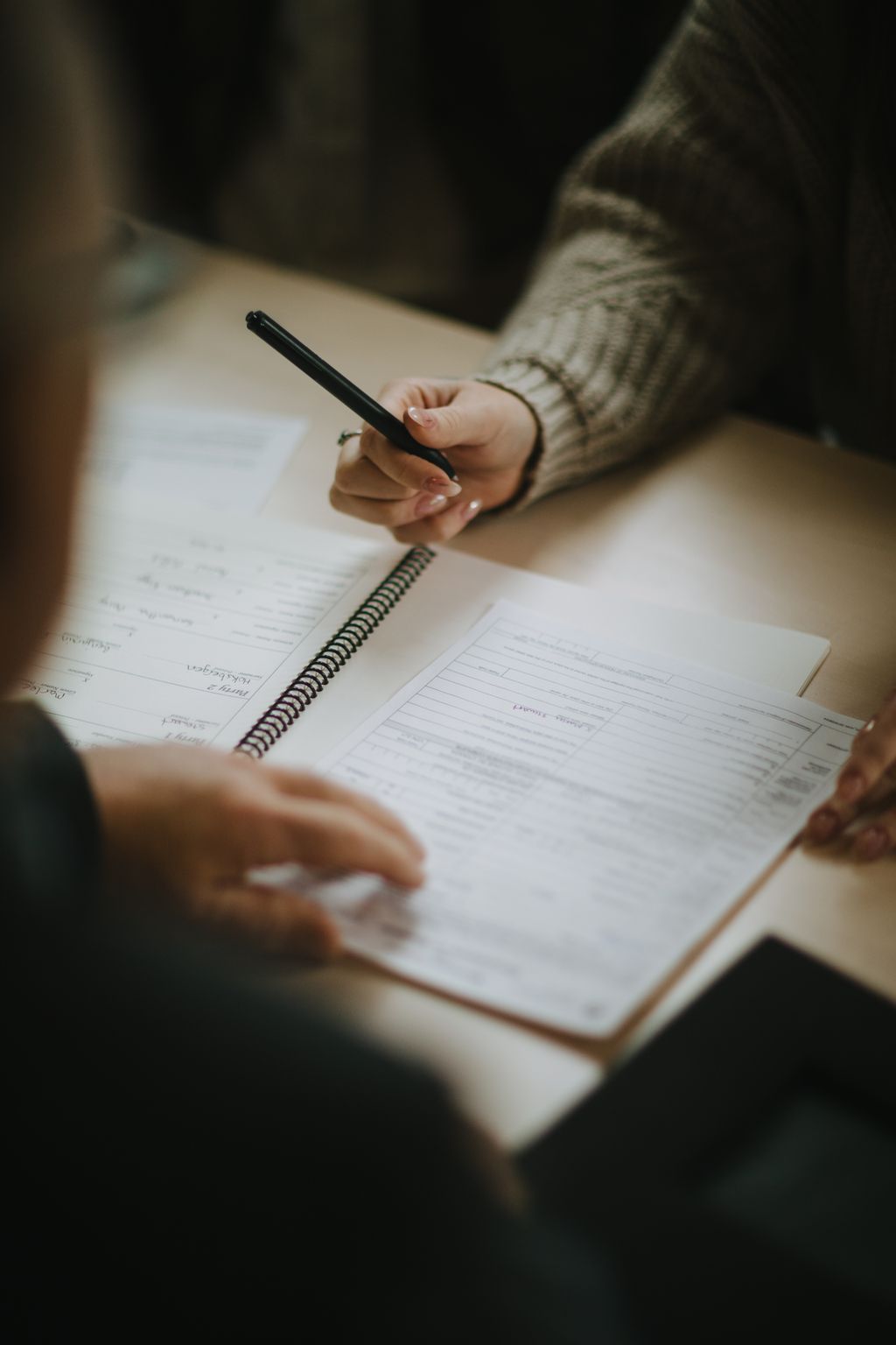 Close-up of hands holding a pen over a spiral notebook during a planning session, warm natural light