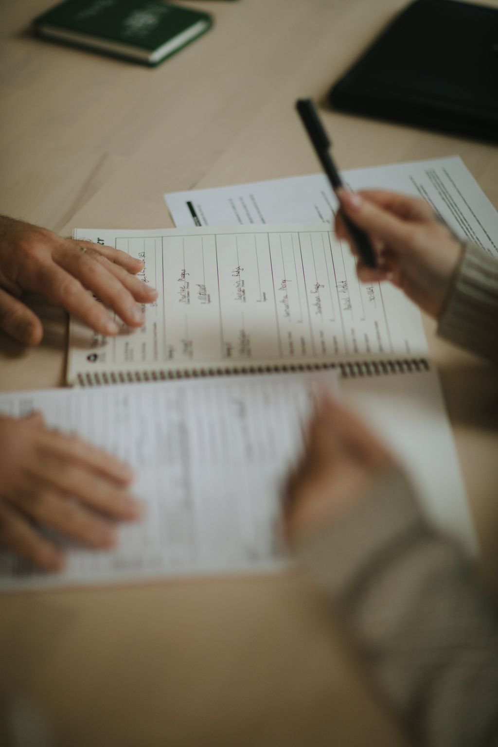 Hands holding a handwritten wedding guest book with a pen, captured in warm natural light on a neutral surface