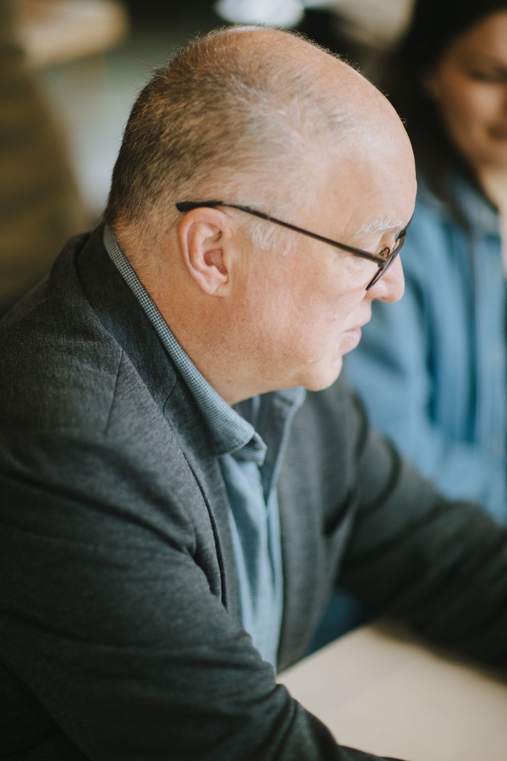 Bespectacled man in light blue shirt photographed in profile, soft natural light highlighting contemplative expression