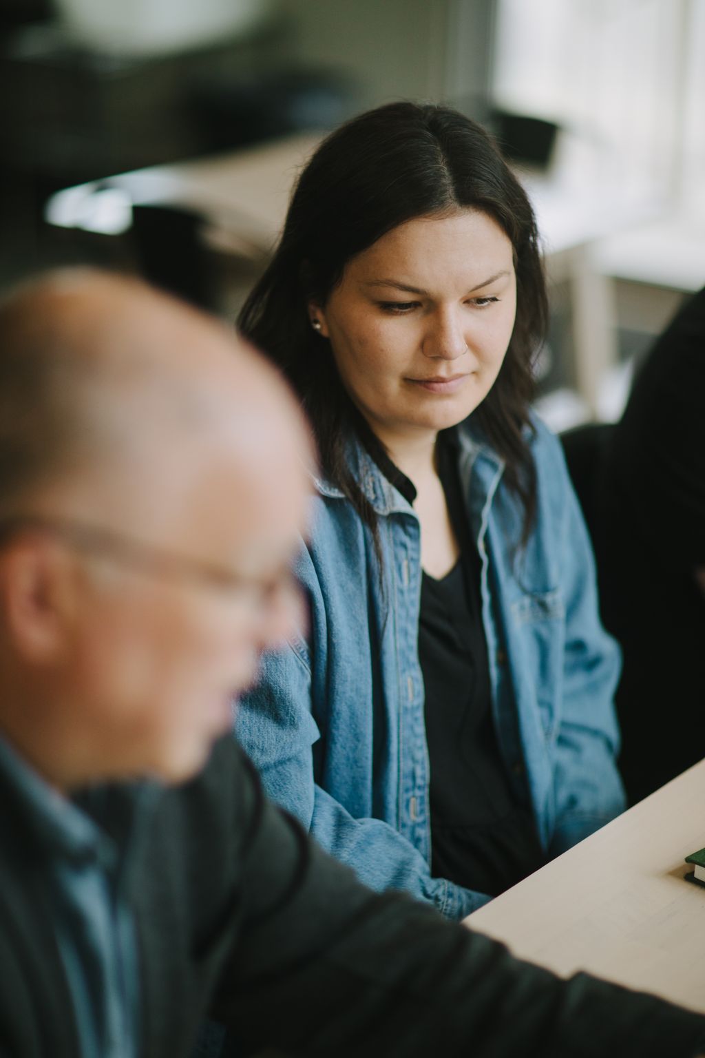 Woman in denim shirt gazing downward with soft natural light and blurred background