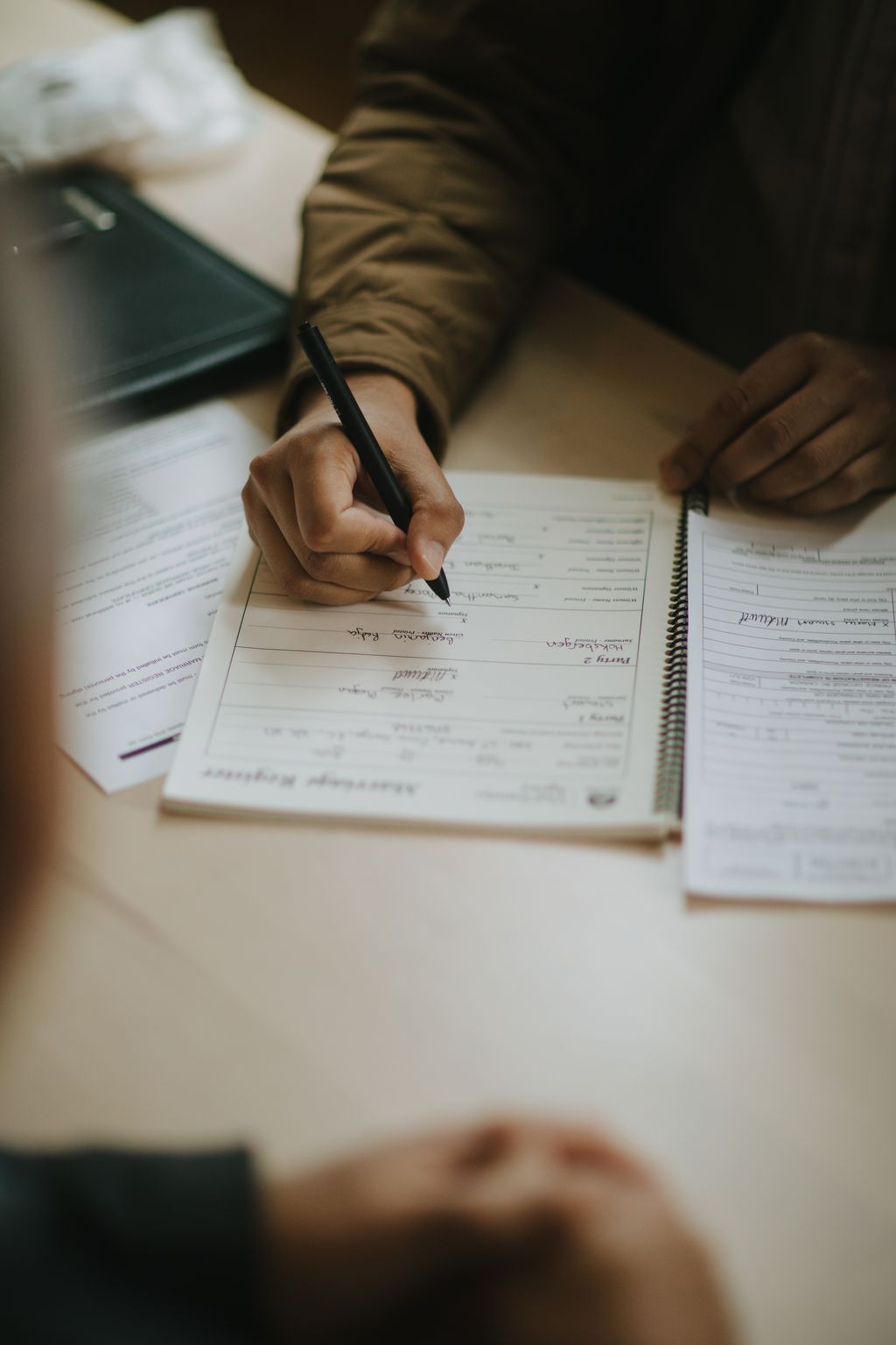 Close-up of a groom''s hand signing a marriage certificate with a black pen during wedding ceremony