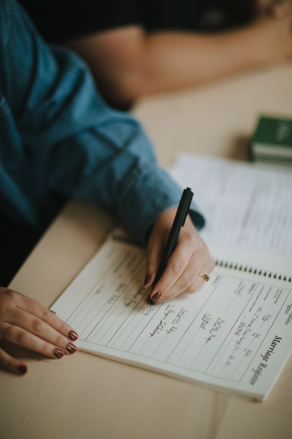 Hand in blue shirt holding pen over wedding guest book with handwritten signatures