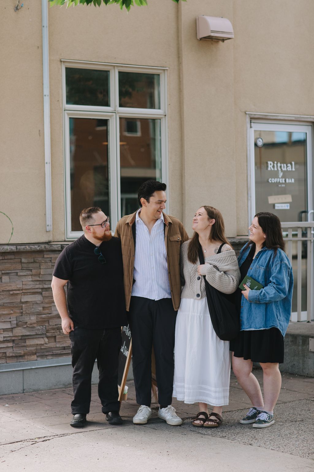 Three people smiling together outside a modern building on a sunny day, casual outdoor portrait