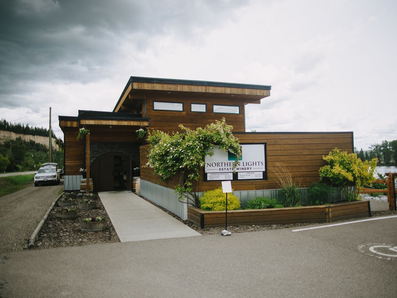 Modern wooden winery building with large windows, lush green vines, and overcast sky, suitable for wedding venue photography