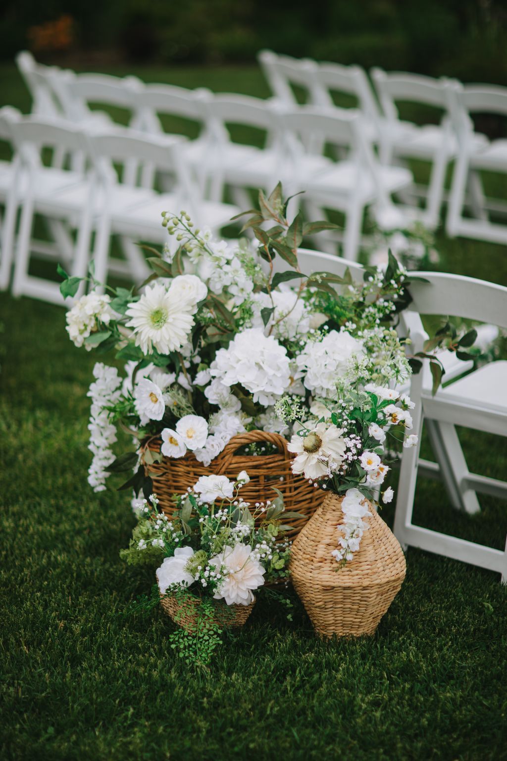 White flowers overflowing from woven baskets on green grass with a white lattice fence backdrop