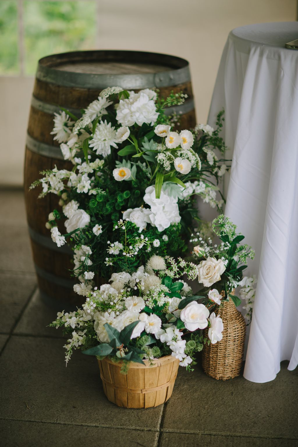 White and cream flowers overflowing from a wooden basket and metal urn create an elegant garden-style wedding arrangement