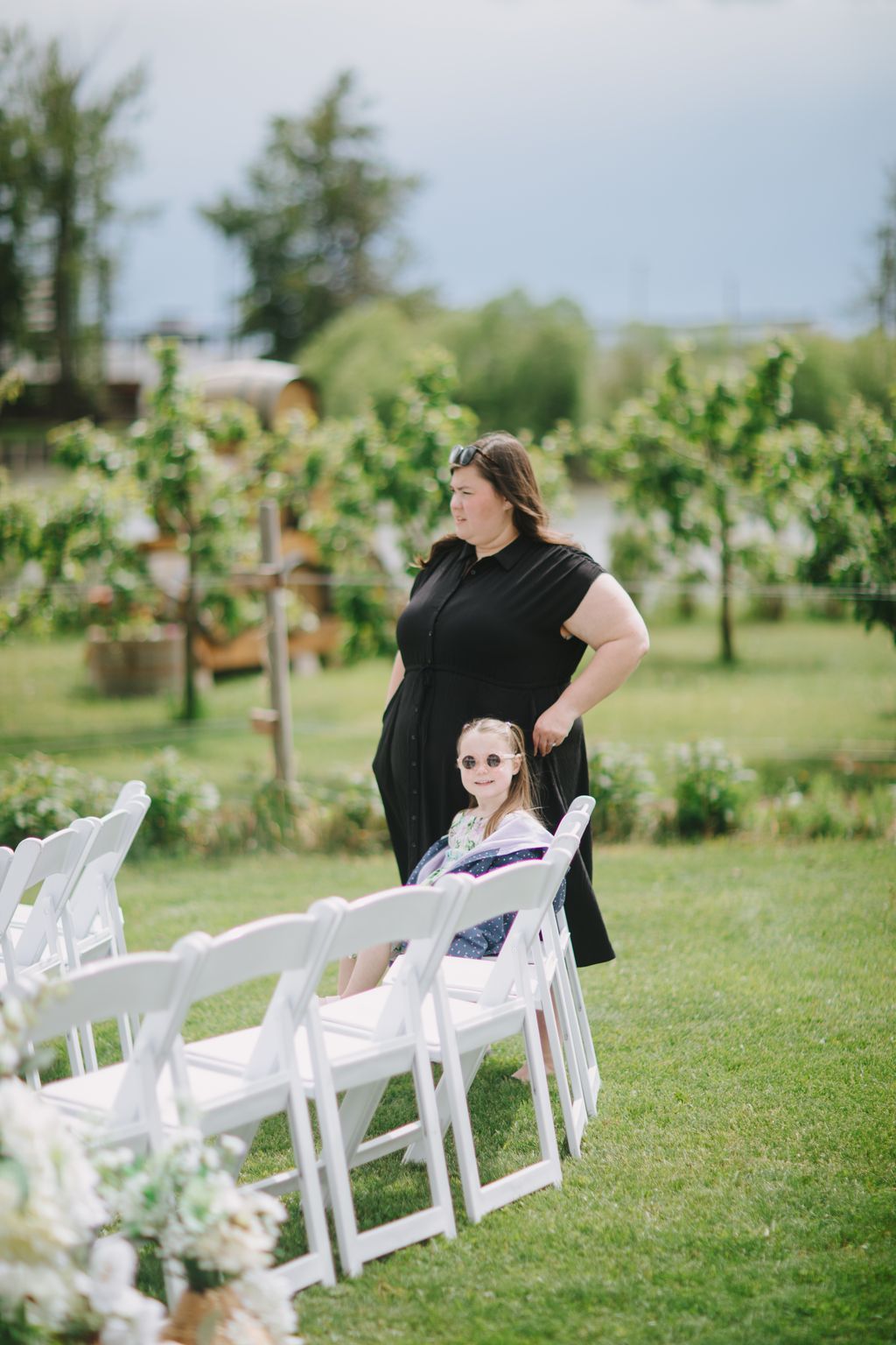 Woman and young girl standing in a garden venue with white ceremony chairs in foreground and lush greenery behind them