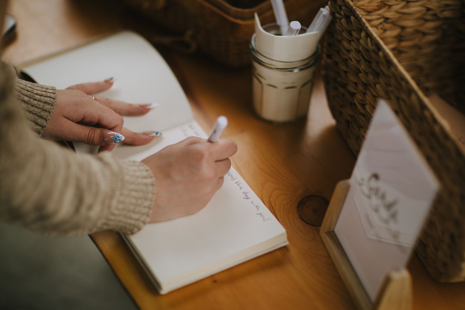 Hand holding pen over handwritten note on wooden table with mason jar and supplies nearby