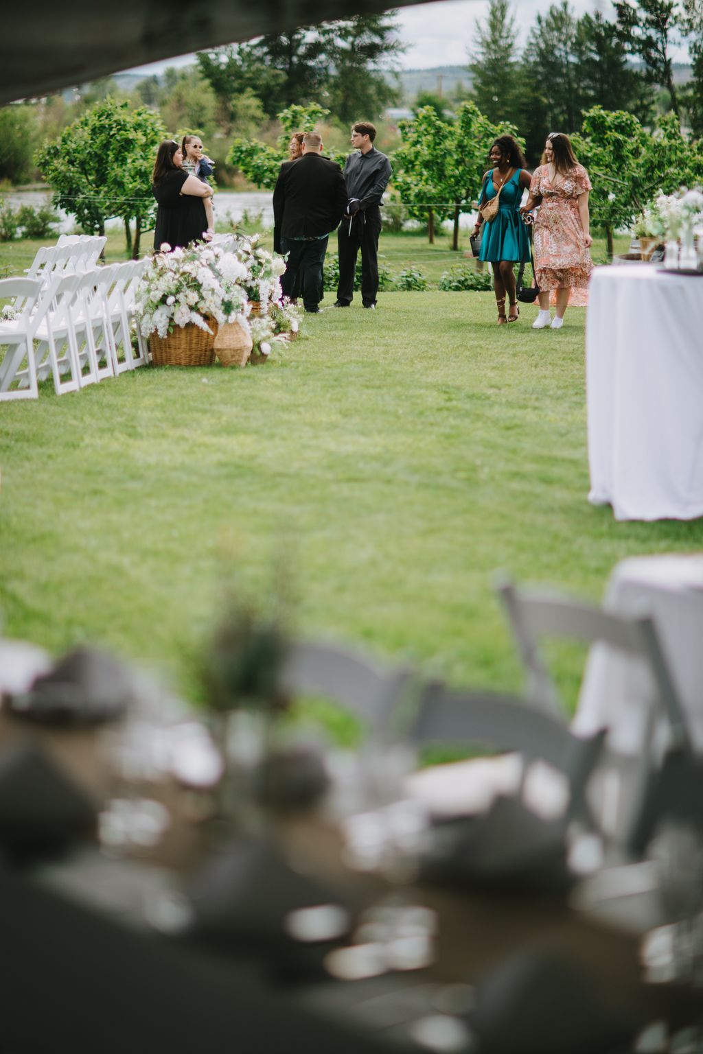 Outdoor garden wedding ceremony with guests gathered on a manicured lawn, white floral arrangements visible, mountains in the distance