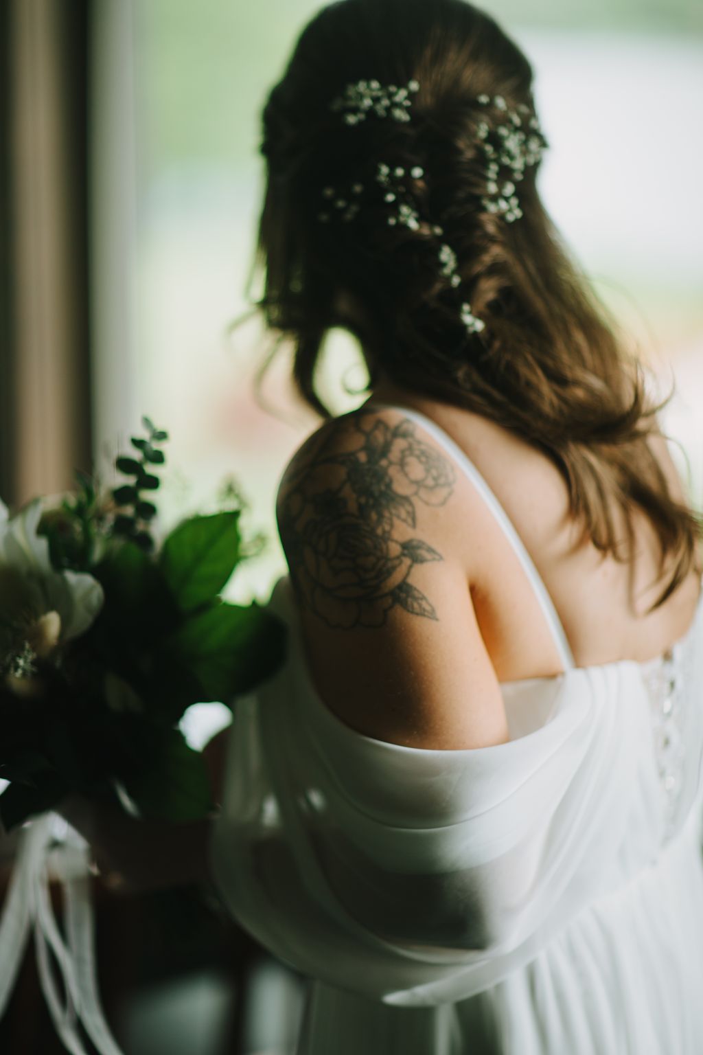 Bride with dark hair adorned with pearl hairpins, showing shoulder tattoo, wearing white dress against soft green background