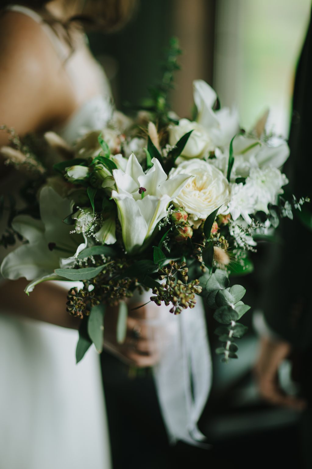 Intimate bridal bouquet of white tulips and garden roses with lush green foliage, held by bride in soft natural light