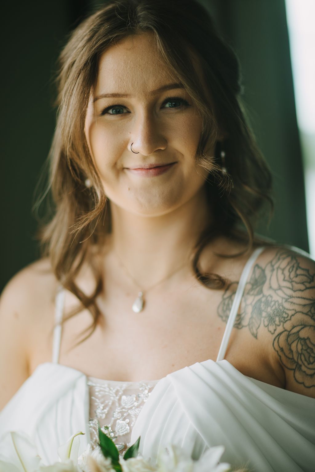 Bride in white lace dress with nostril piercing smiles warmly in soft, golden natural light