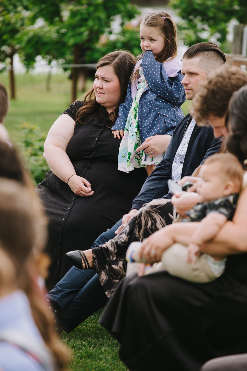 Woman and young girl sitting on grass at outdoor wedding celebration, smiling together in natural daylight