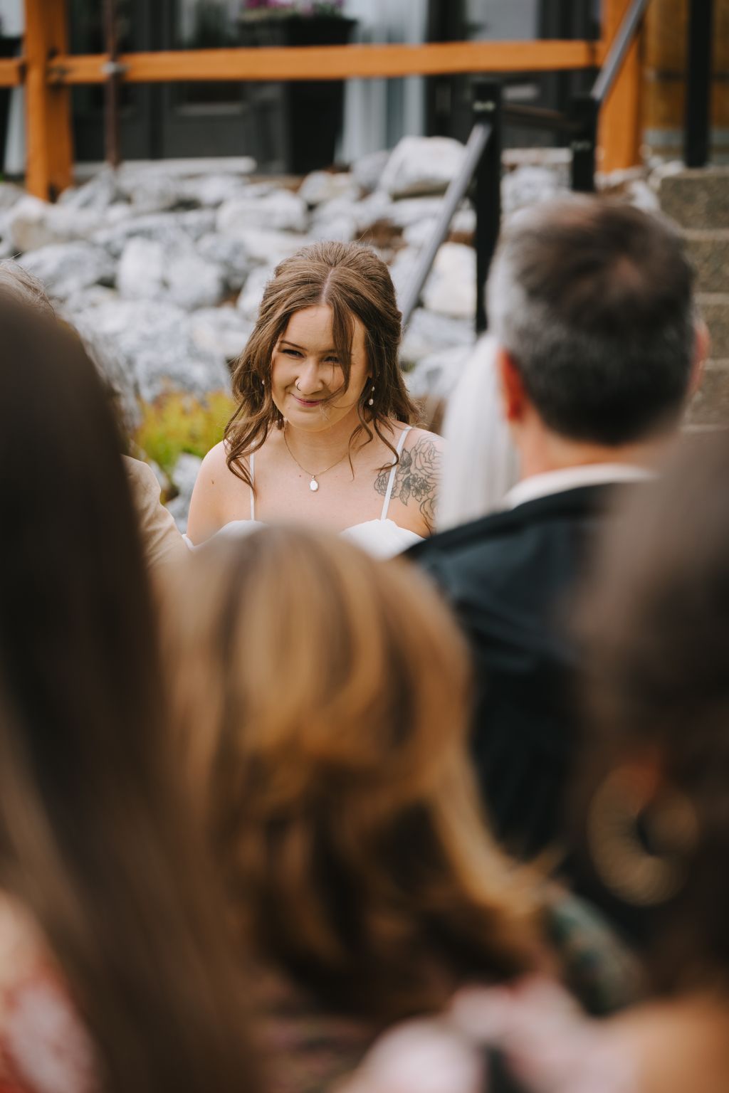Bride smiling warmly during outdoor ceremony with white chairs and wooden structure in soft daylight