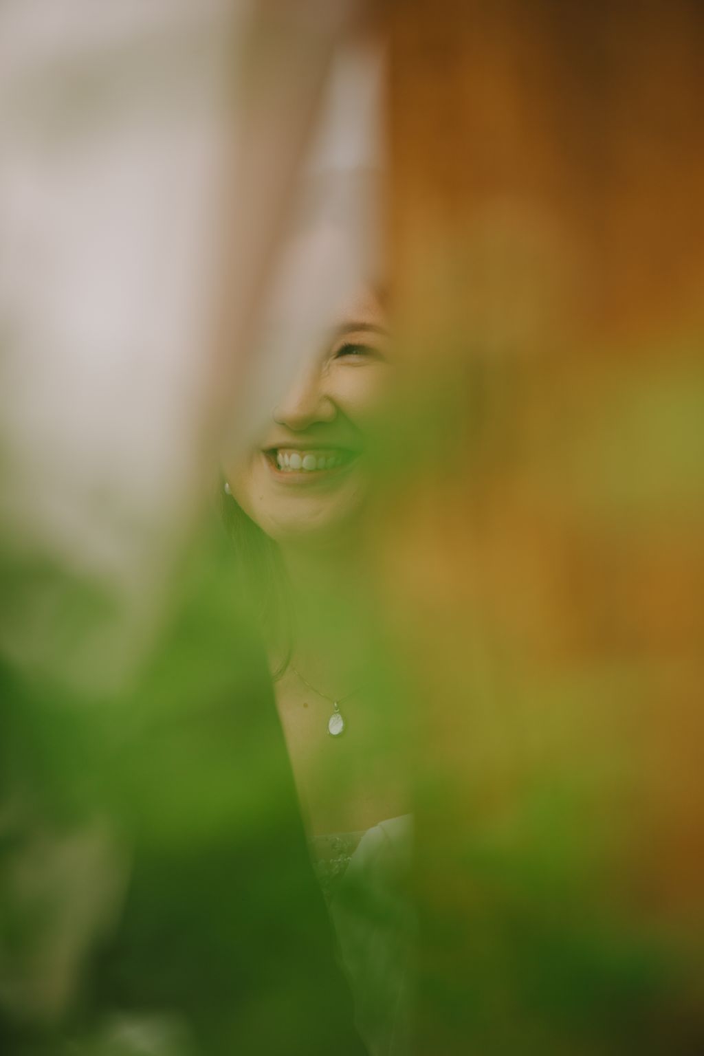 Smiling woman in green tones with soft focus and warm golden light, wearing a pendant necklace