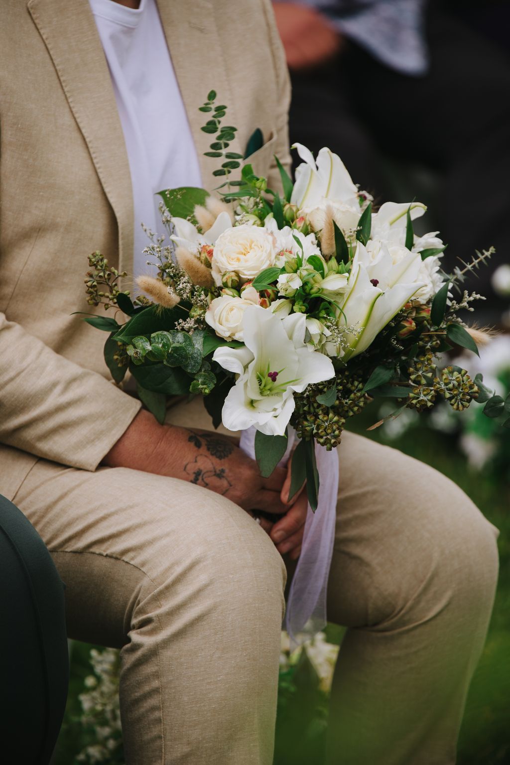 Bride in cream linen holding white rose and ranunculus bouquet with greenery and lavender ribbon