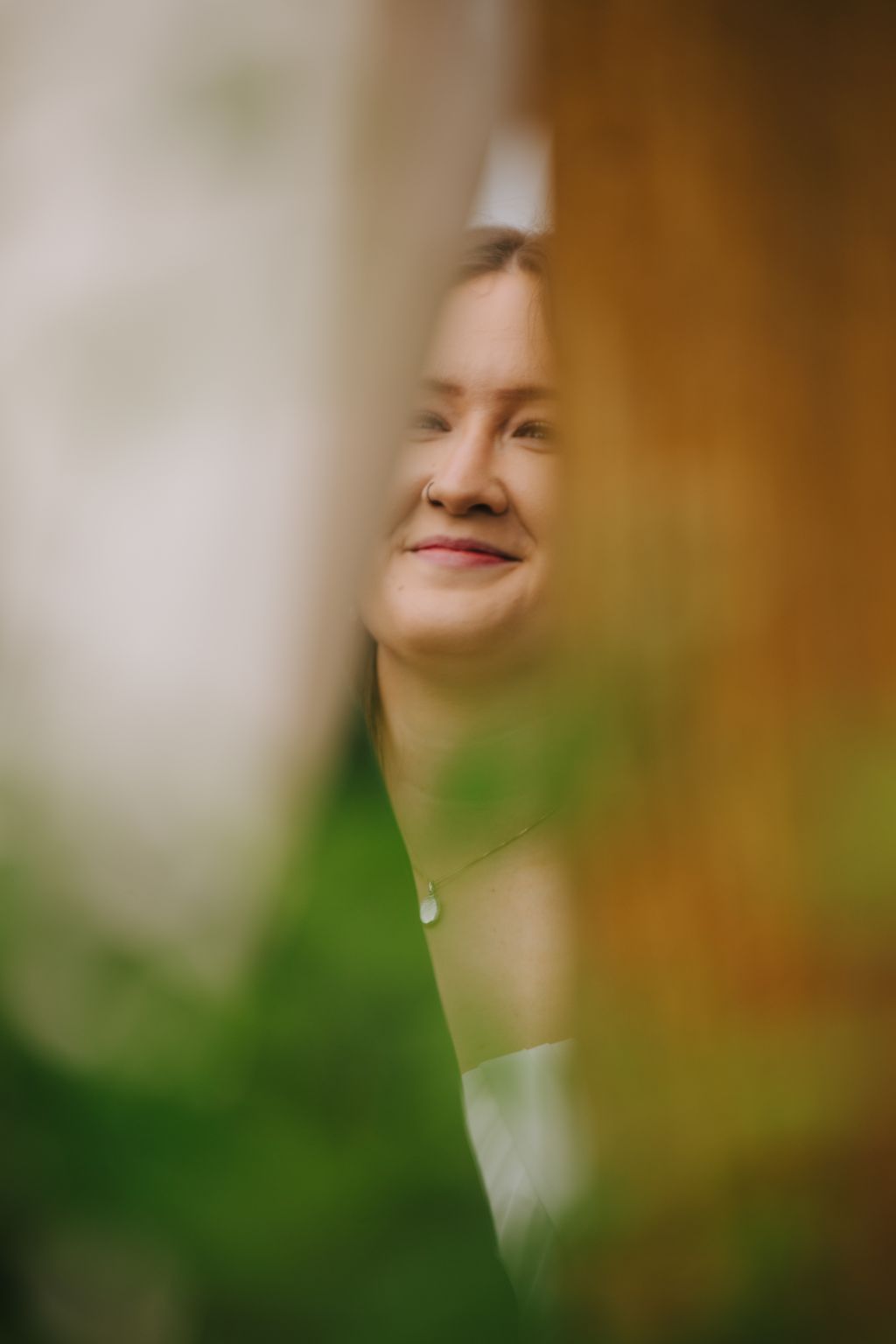 Woman with eyes closed wearing a pendant necklace, soft-focused natural background in warm and green tones