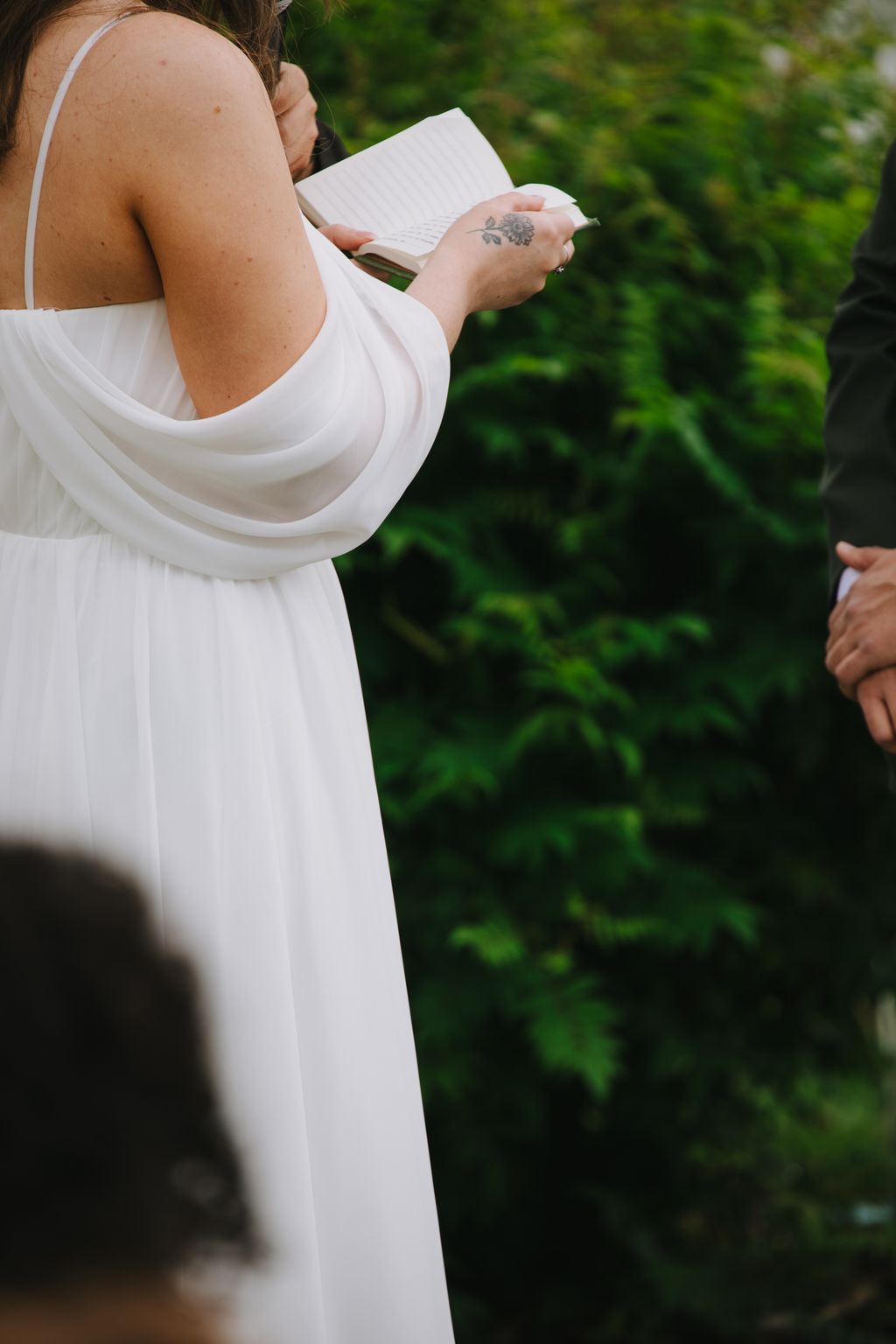 Bride in white dress holding vows outdoors with soft green foliage background