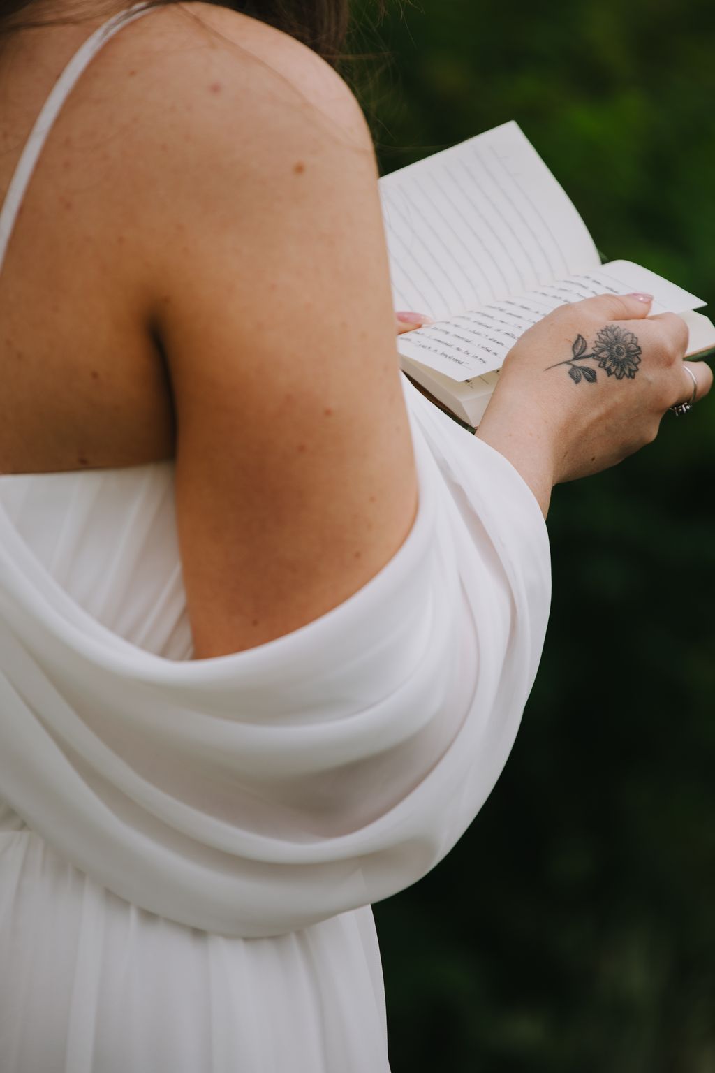 Bride in white dress holding handwritten vows, outdoor natural light with soft focus green background