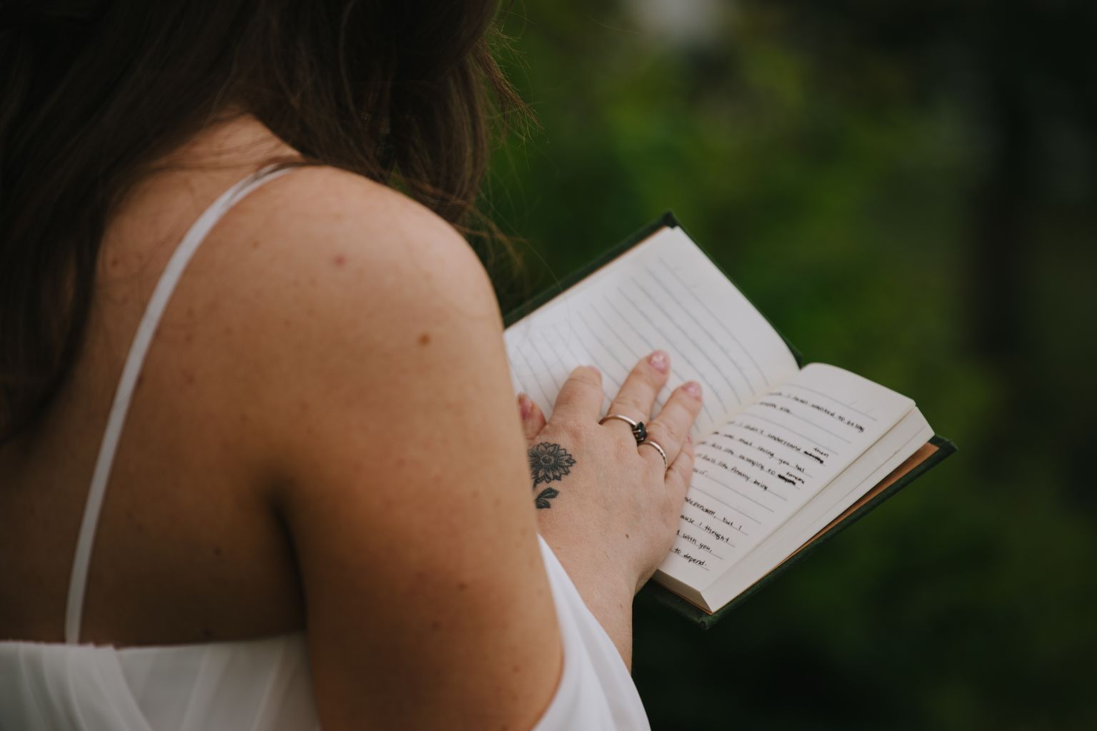 Woman with dandelion tattoo on hand holding open notebook outdoors with soft green background