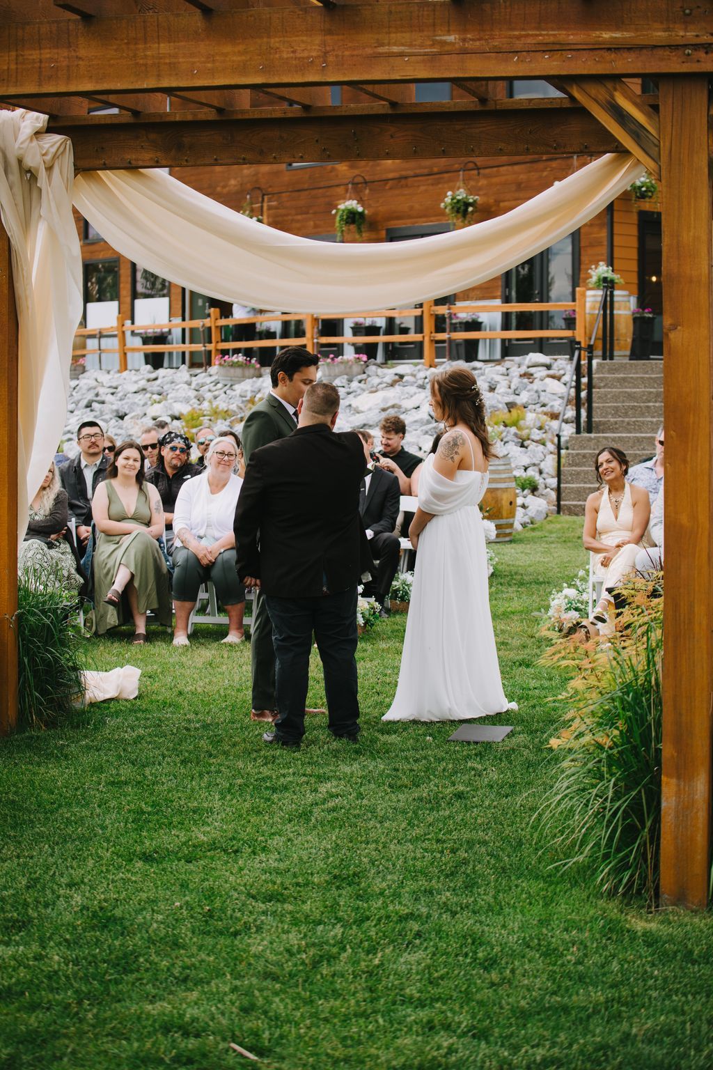 Bride and groom exchange vows under draped fabric canopy with wooden beams and hanging florals during outdoor ceremony