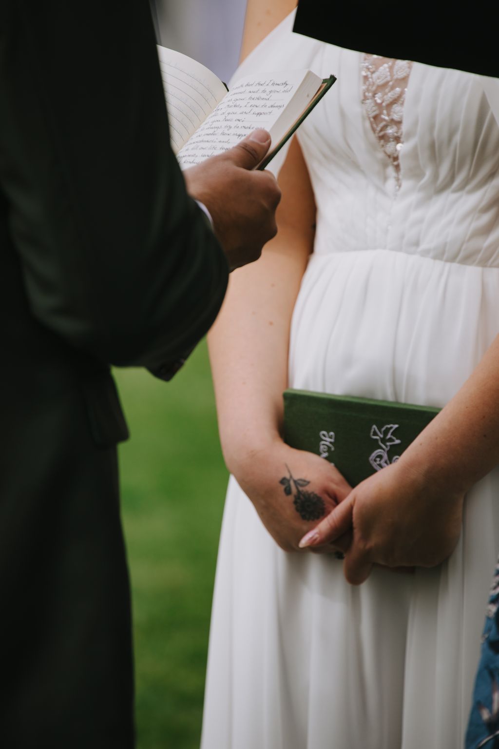Bride and groom exchange handwritten vows from an open notebook during outdoor ceremony with green background