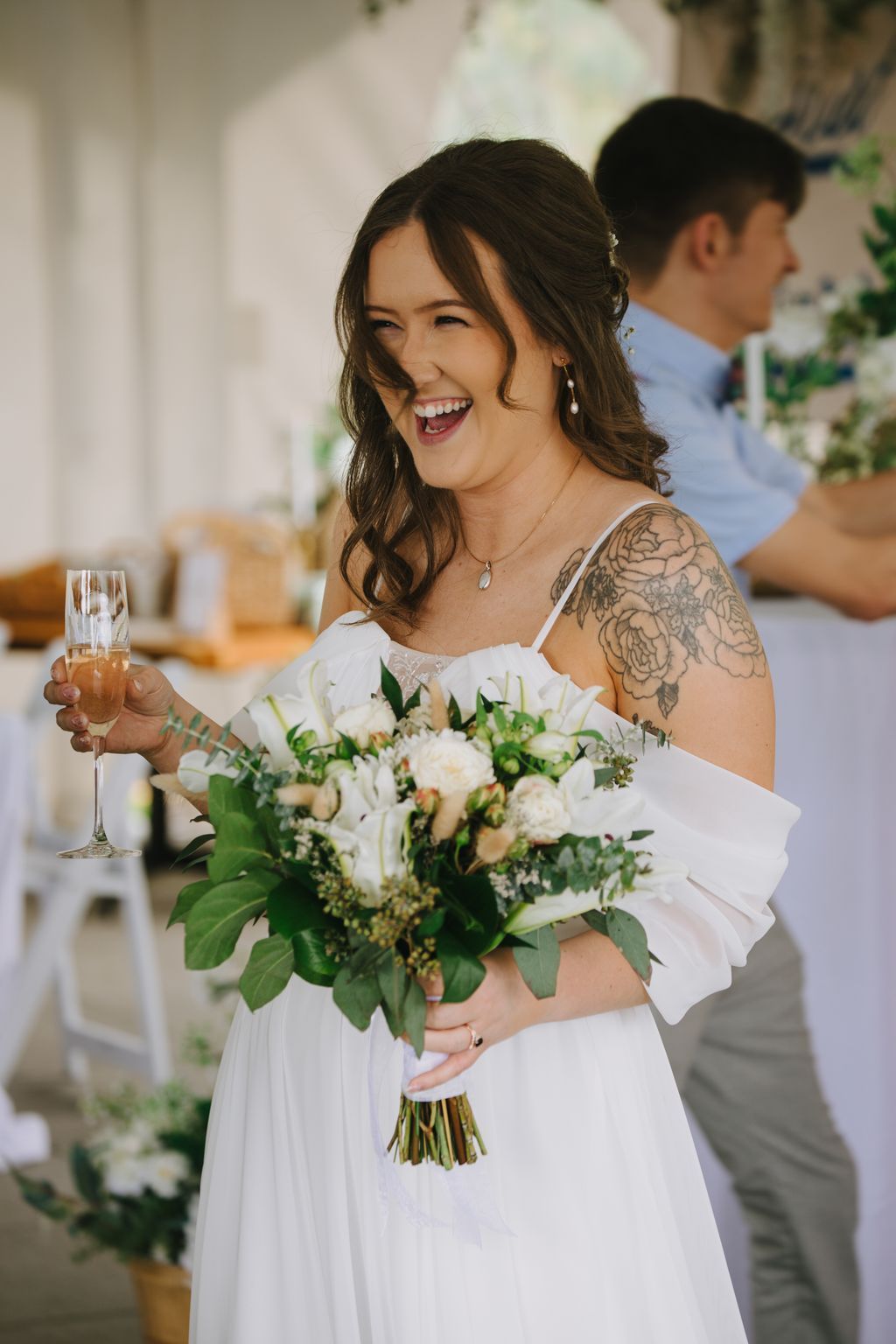 Joyful bride in white dress holding white and green bouquet, laughing with genuine happiness on her wedding day