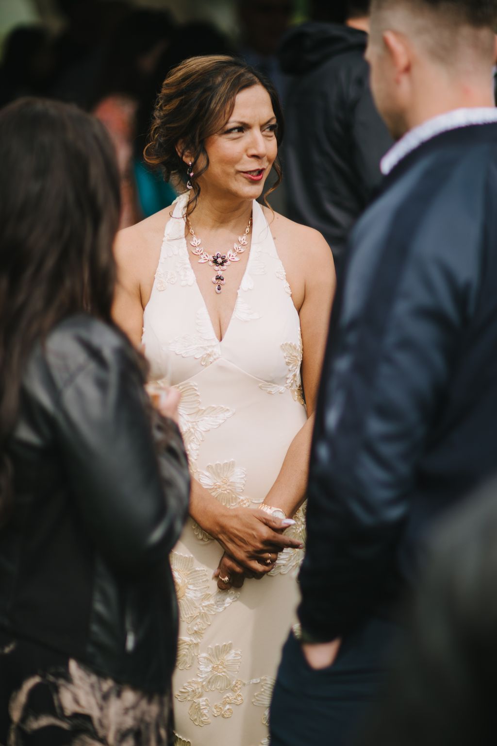 Elegant bride in beaded cream halter gown with ornate silver necklace, smiling at outdoor evening reception