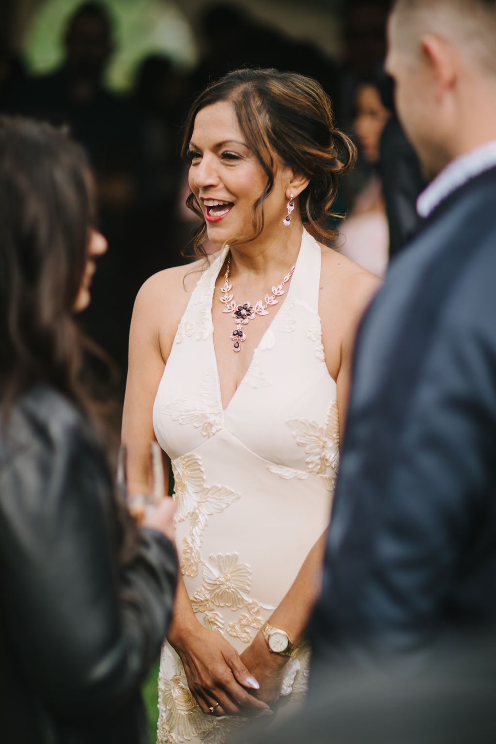Bride in ivory halter dress with floral embroidery smiles during ceremony, wearing amethyst necklace and earrings