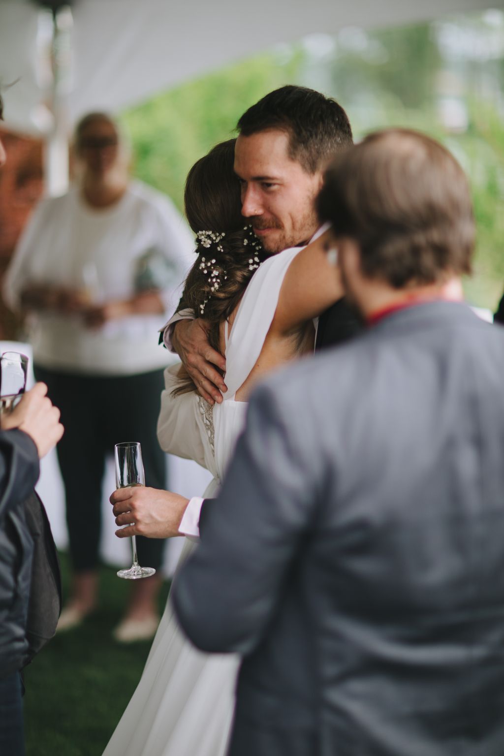 Groom in white shirt embraces bride in white dress with floral hair detail during outdoor wedding reception