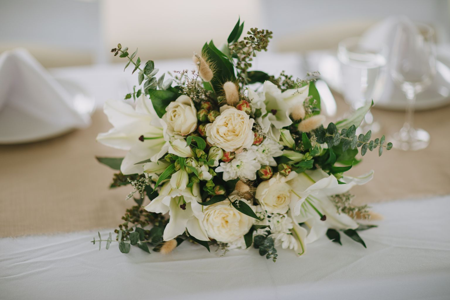Elegant bridal bouquet of cream roses, white flowers, and green foliage with textured leaves against a soft white background