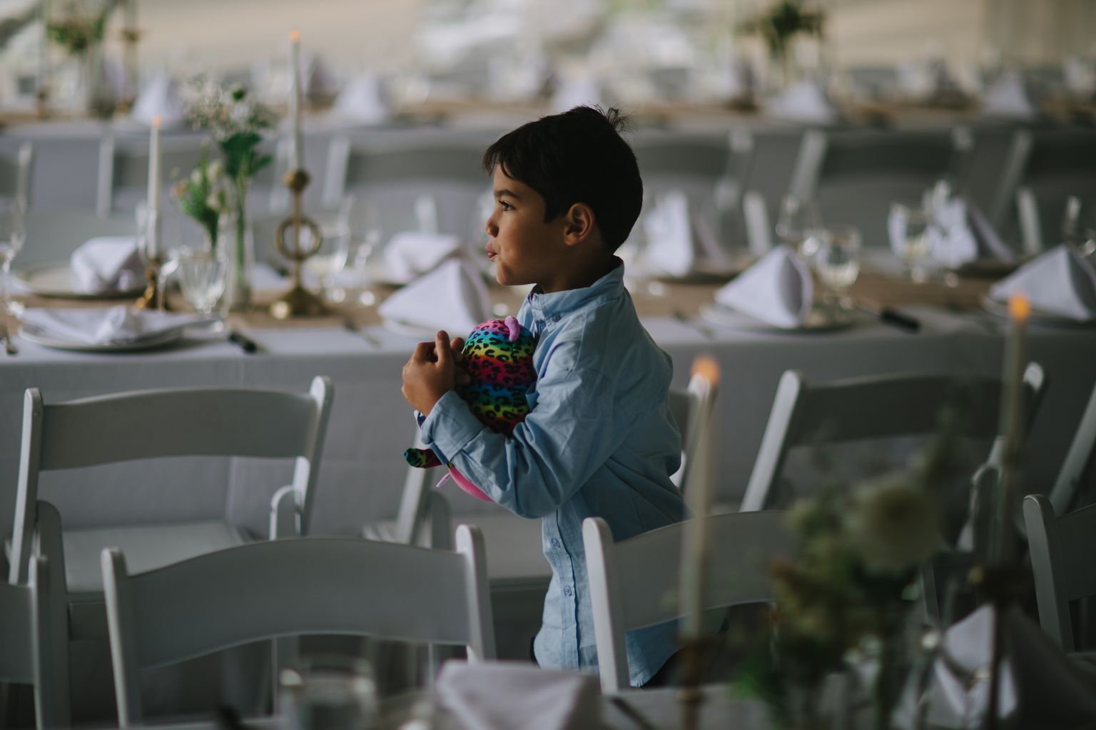 Young boy in light blue shirt holding colorful toy ball, standing indoors with soft natural light and blurred background