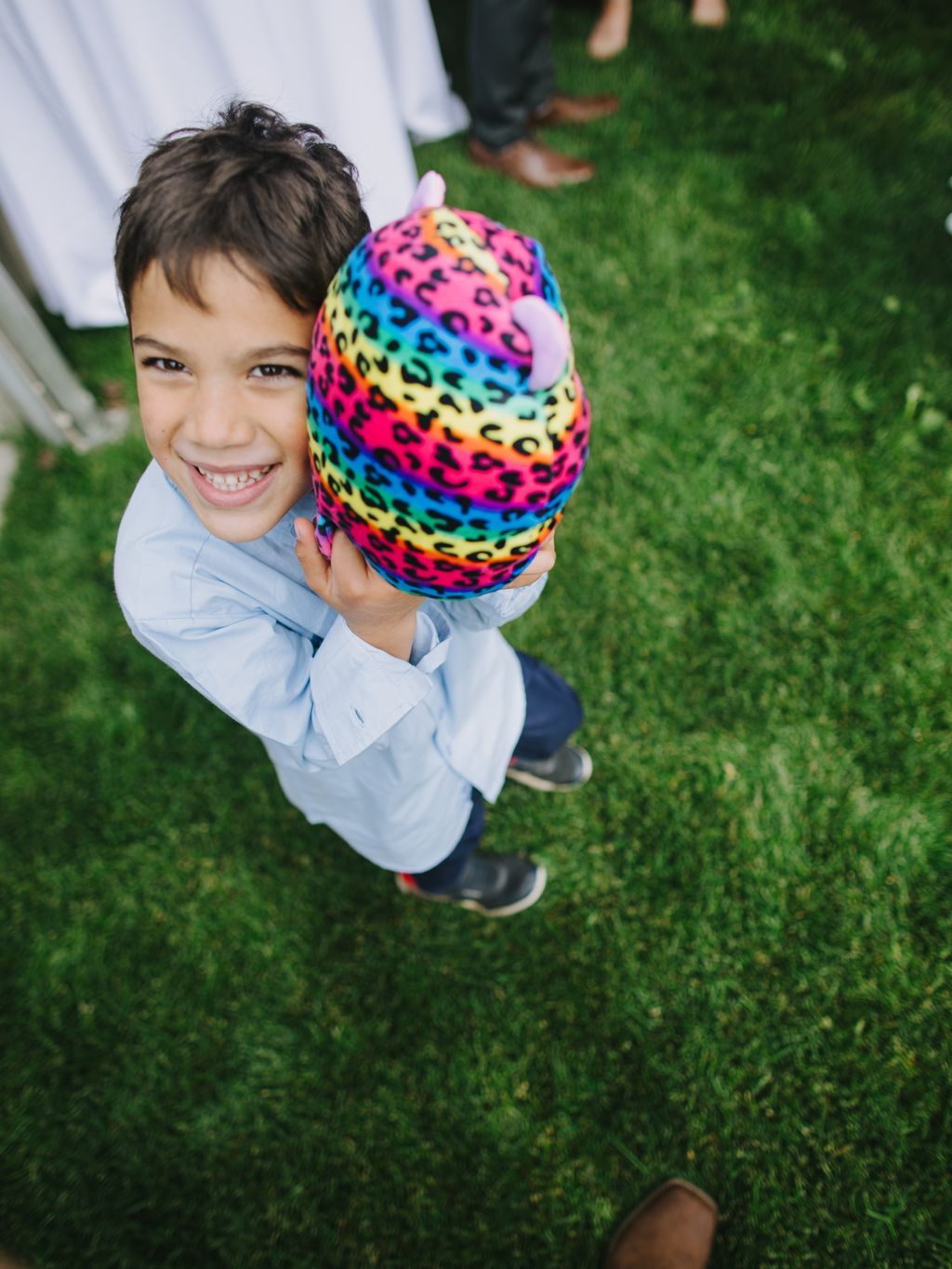 Child holding colorful neon leopard print ball smiling at outdoor wedding celebration on grass
