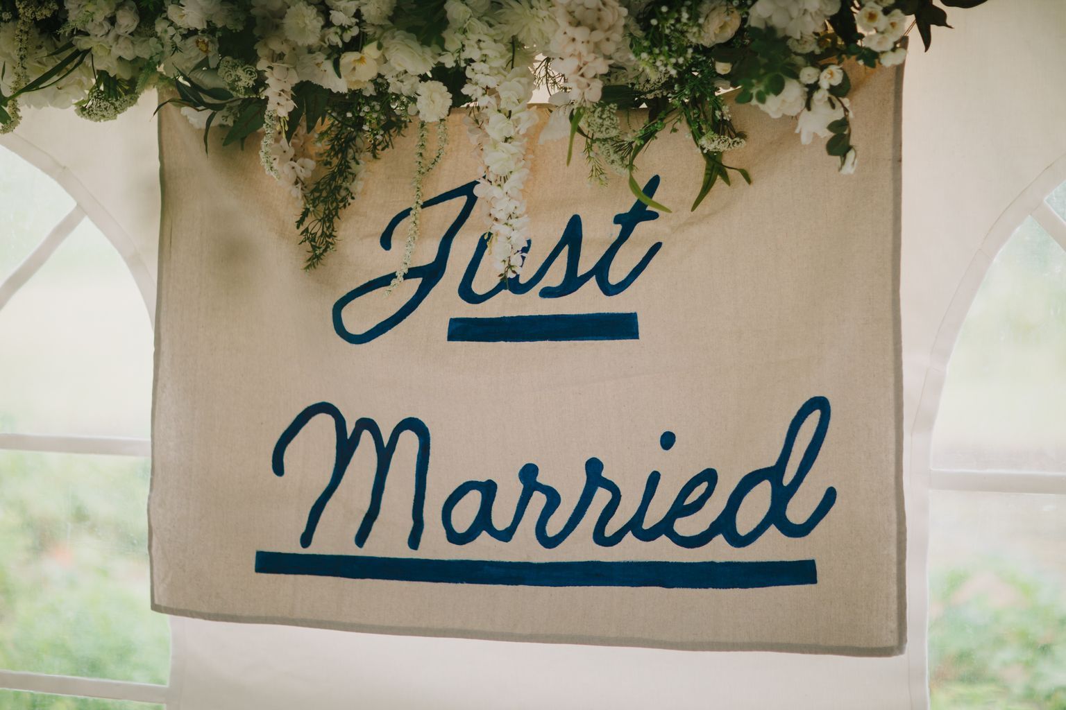 Hand-lettered wedding sign reading "Just Married" in navy script with white flowers and cascading greenery overhead
