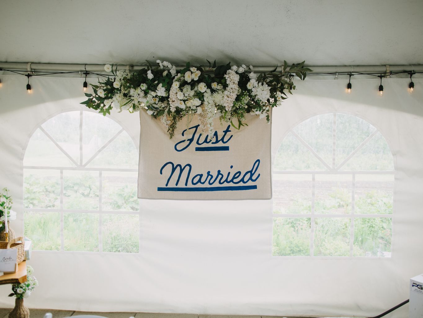 Just Married" banner with white flowers and greenery hanging from metal rod against white wall