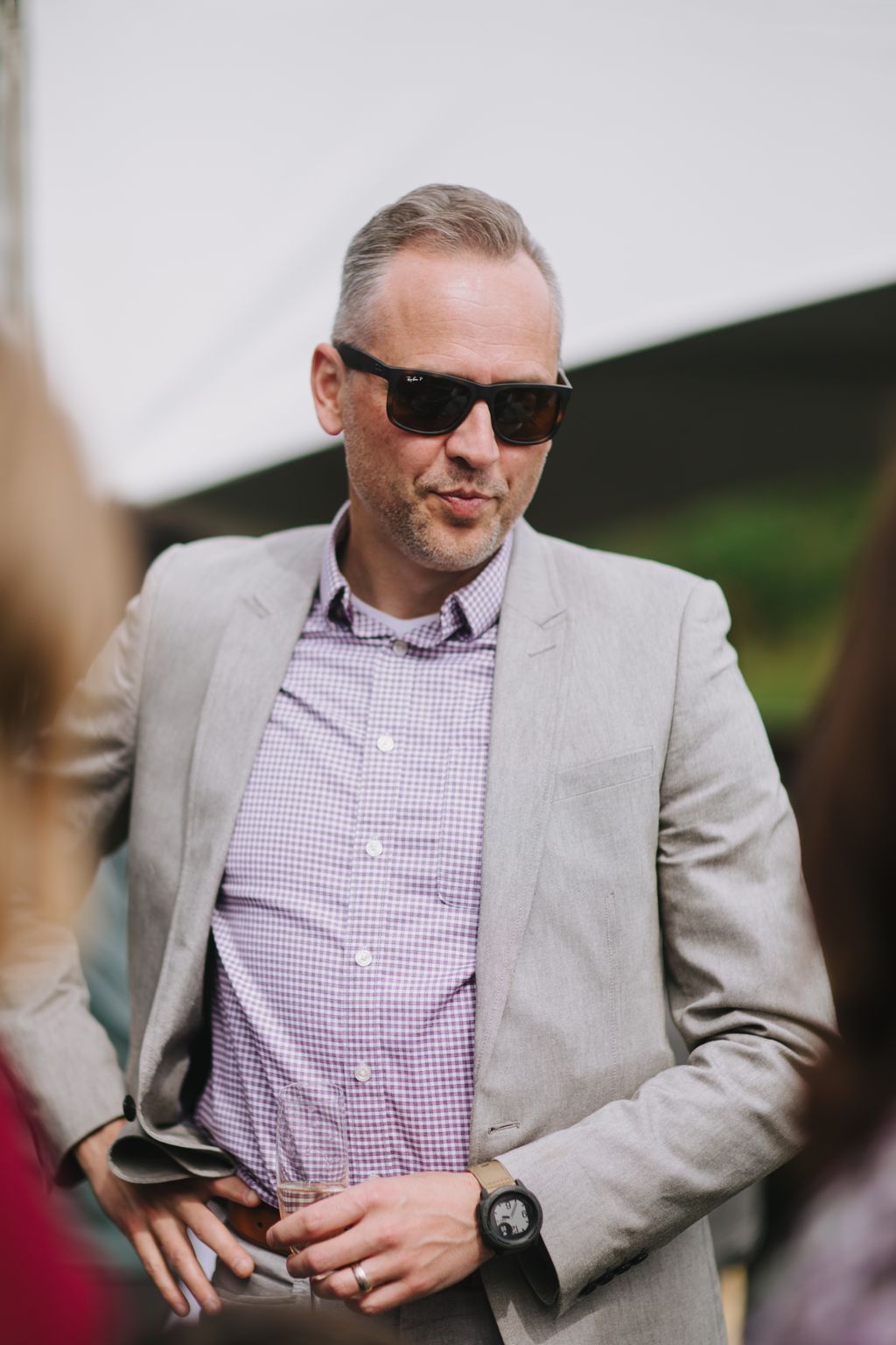 Groom wearing sunglasses and lavender gingham shirt with gray blazer, smiling outdoors in natural light