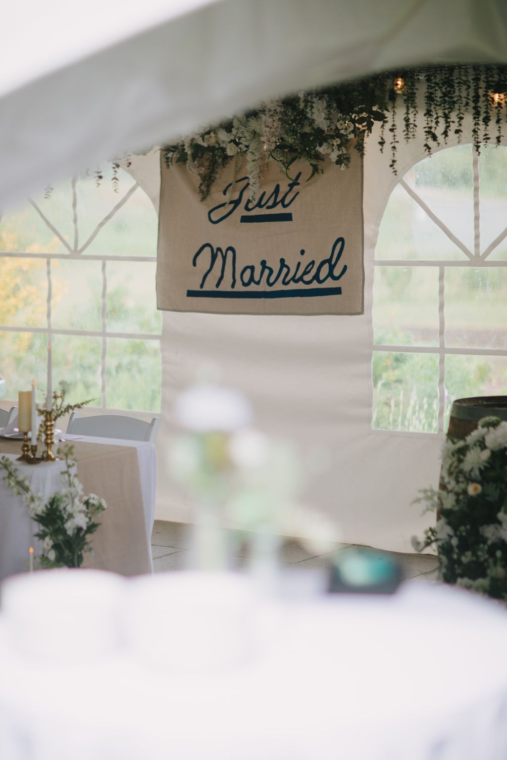 Burlap "Just Married" banner with green garland hanging from white ceiling at wedding reception entrance