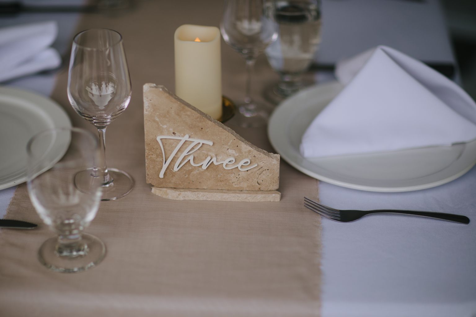 Elegant table setting with "Three" carved in stone, lit candle, glassware, and place setting in warm natural light