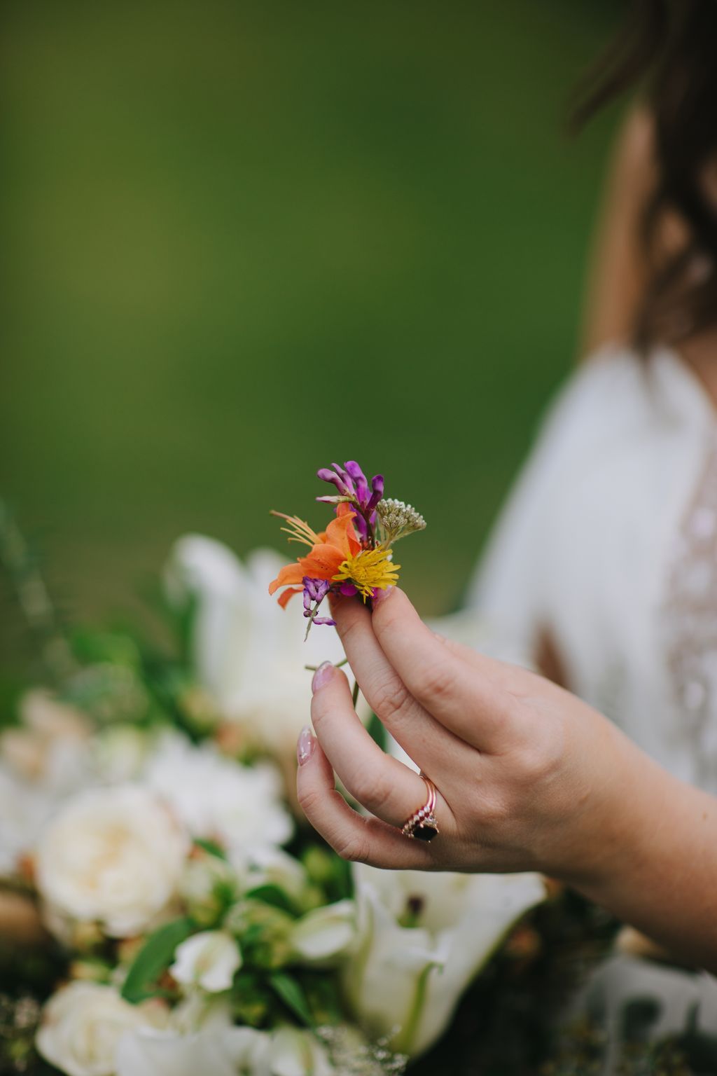 Bride''s hand holding vibrant wildflowers with delicate ring, soft green garden backdrop