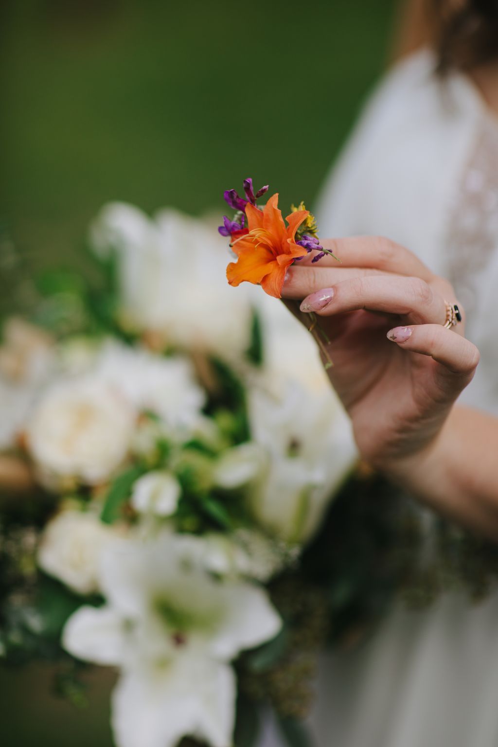 Delicate orange flower with purple buds held in a bride''s hand against a soft green and white blurred background