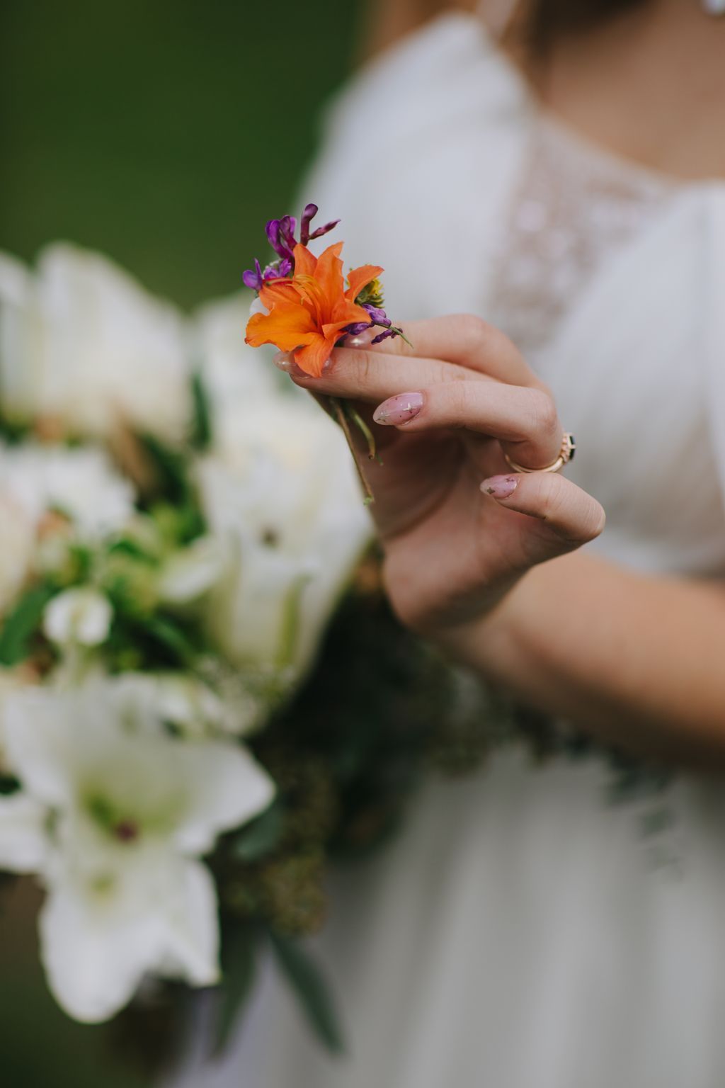 Bride''s hand holding vibrant orange and purple flower with manicured nails, soft green background