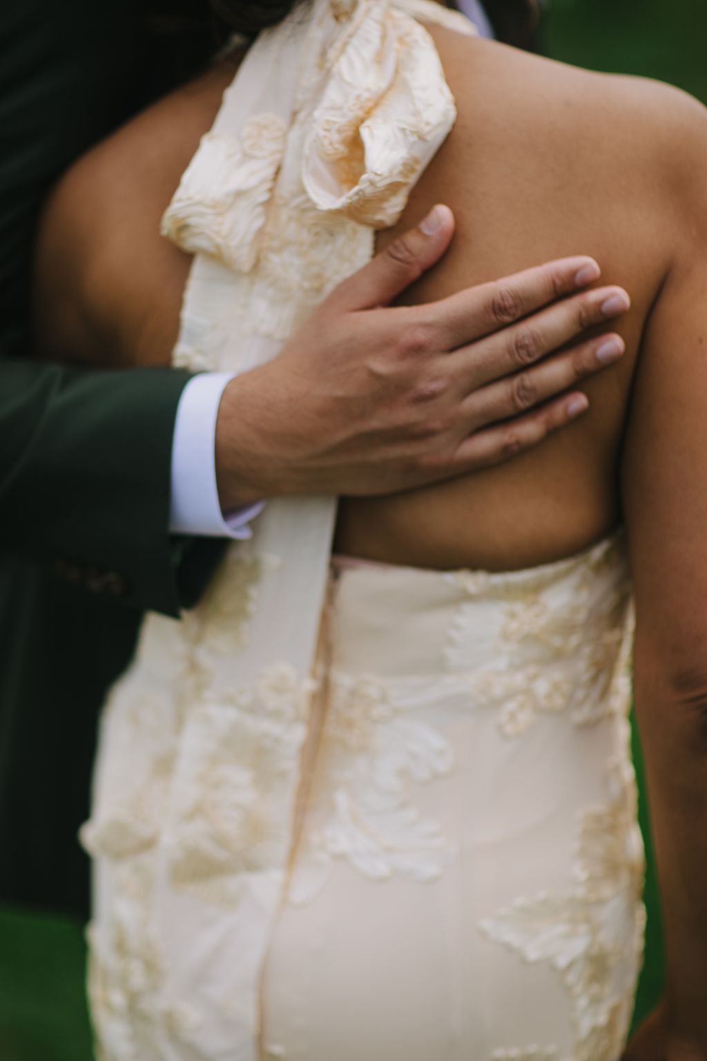 Groom''s hand on bride''s lace-detailed wedding dress, intimate close-up detail shot
