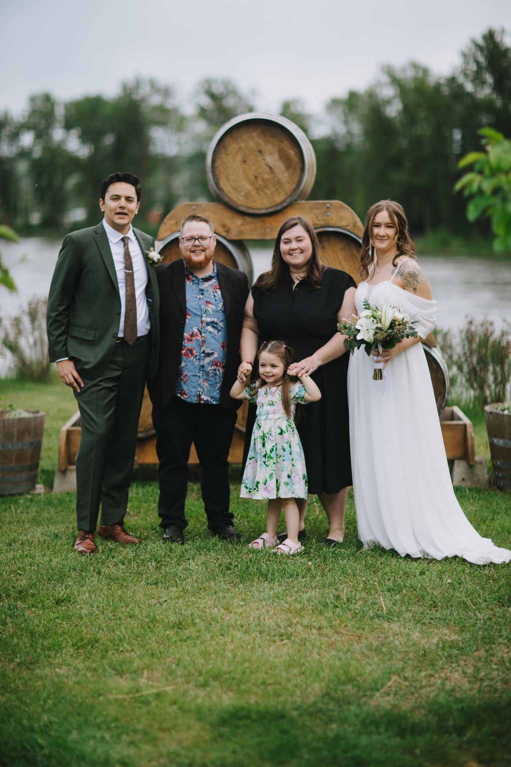Family group posing on grass in front of wooden barrels at an outdoor wedding venue
