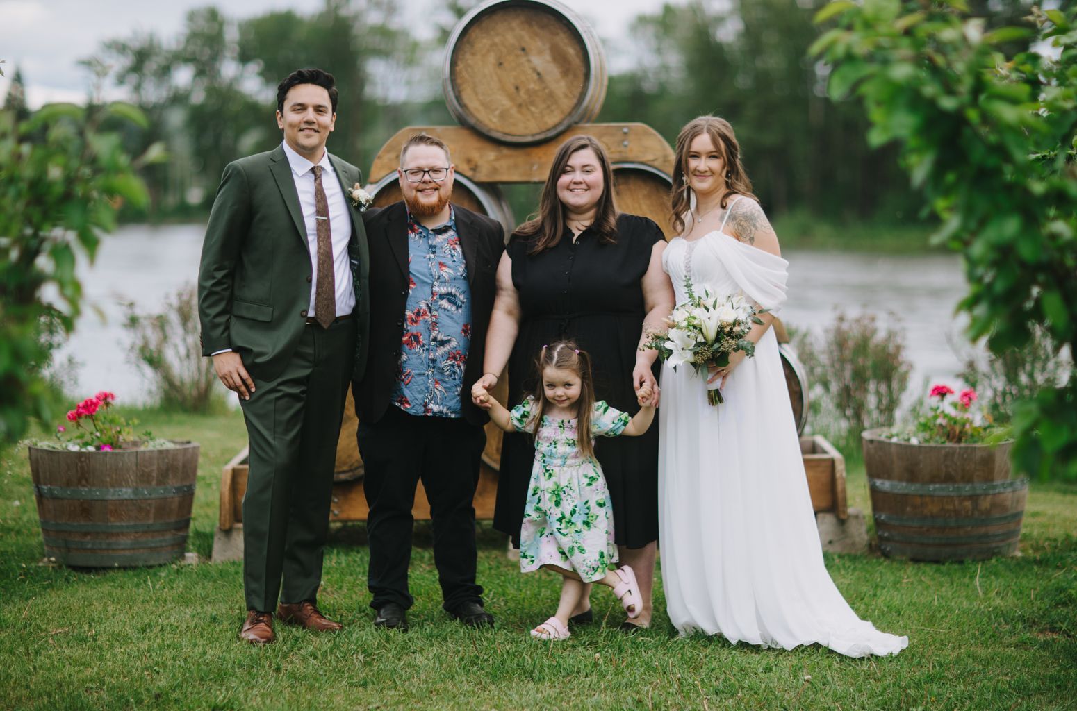 Family of four smiling at camera in front of wooden barrels, soft natural light, green grass setting