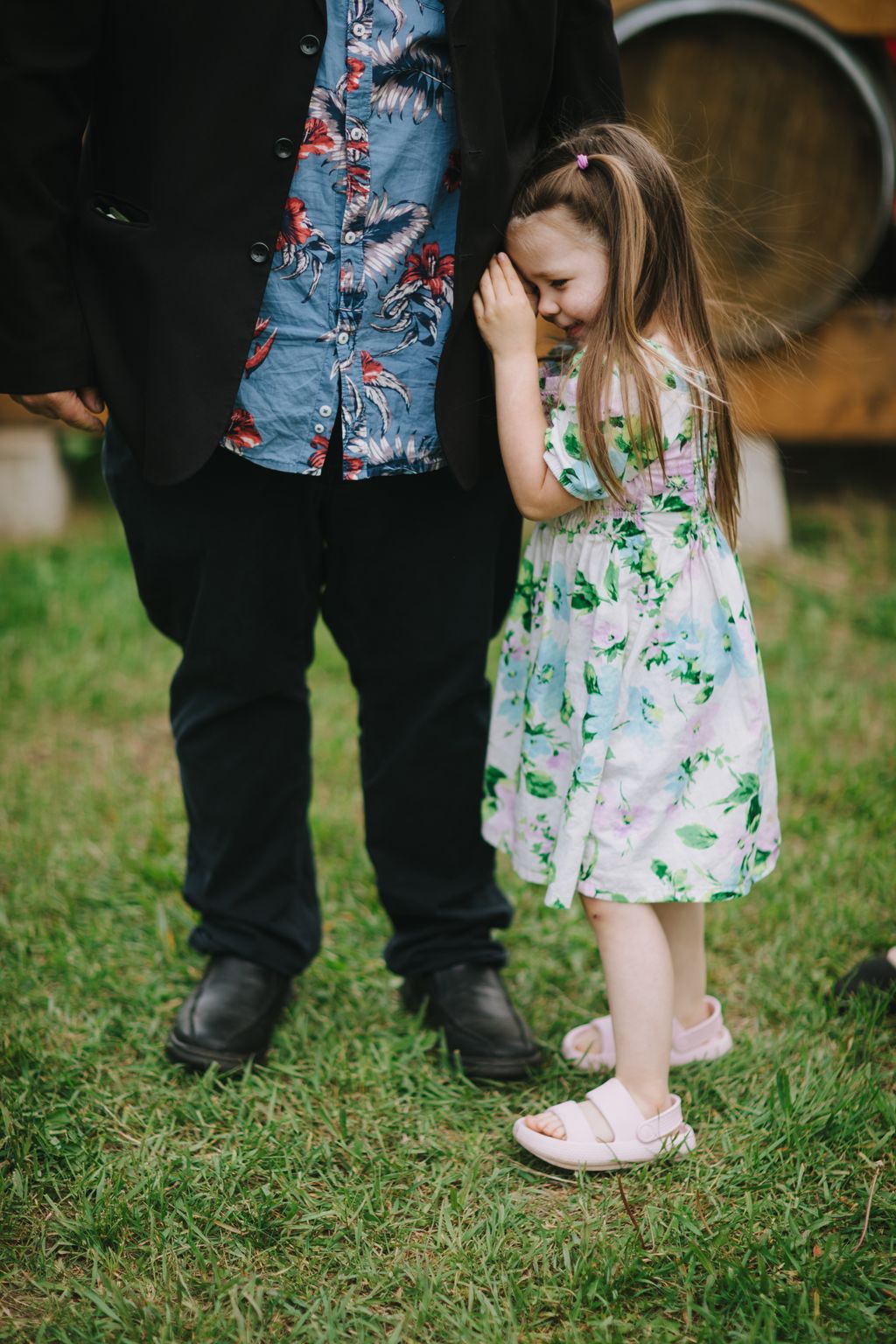 Young girl in floral dress stands beside couple on grass during outdoor wedding celebration