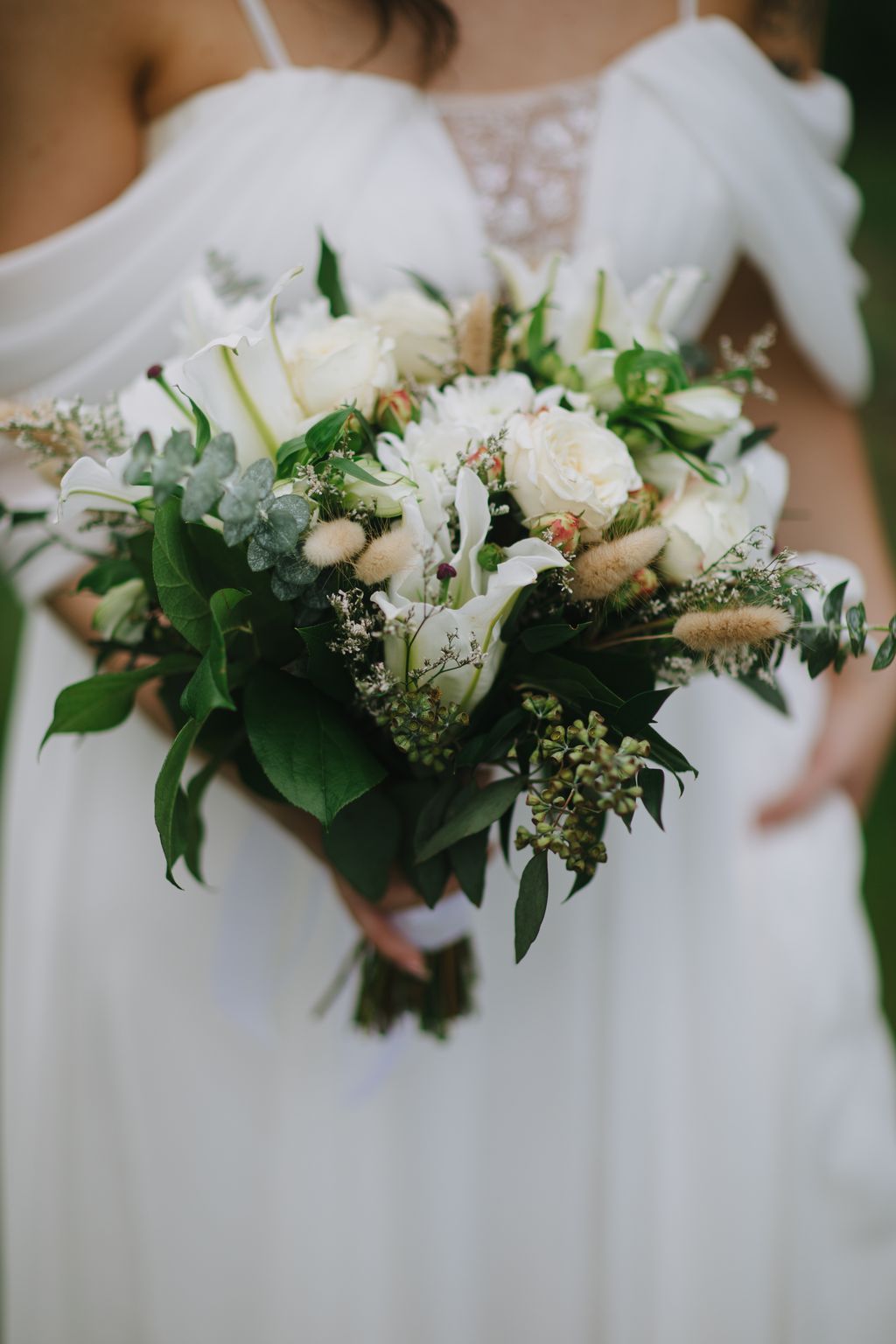 Bride in white lace gown holding romantic bridal bouquet of cream roses, white calla lilies, and textured greenery
